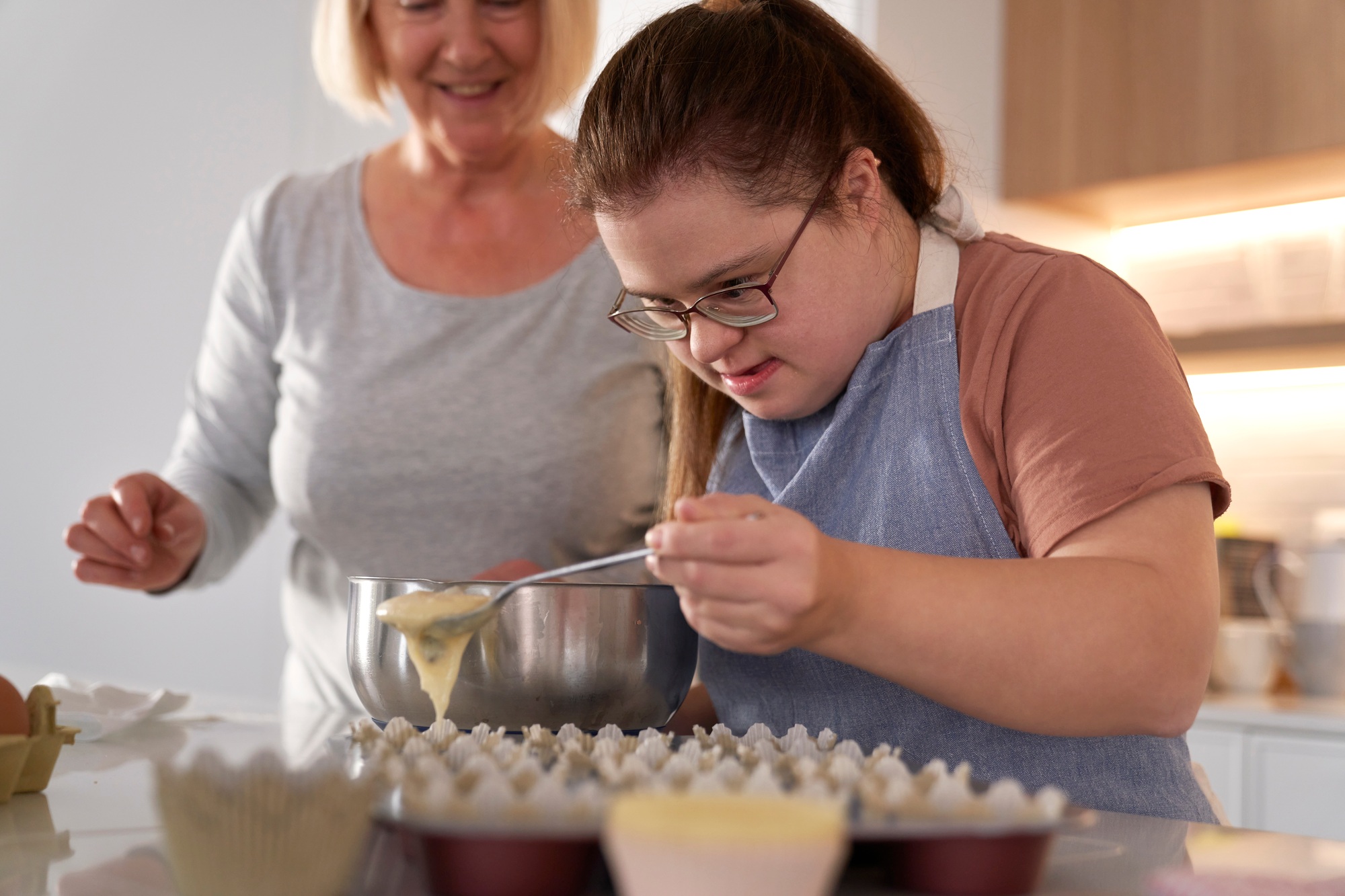 Young woman baking with assistance as part of NDIS life skills program at Caring Humanity